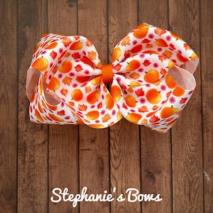 May include: A large orange and white bow with a pumpkin and leaf pattern. The bow is tied with a bright orange ribbon.