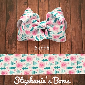 May include: A 6-inch hair bow with a white background and a repeating pattern of pink and teal Christmas trees. The bow is made of ribbon and has a large, layered design. The text "Stephanie's Bows" is at the bottom.