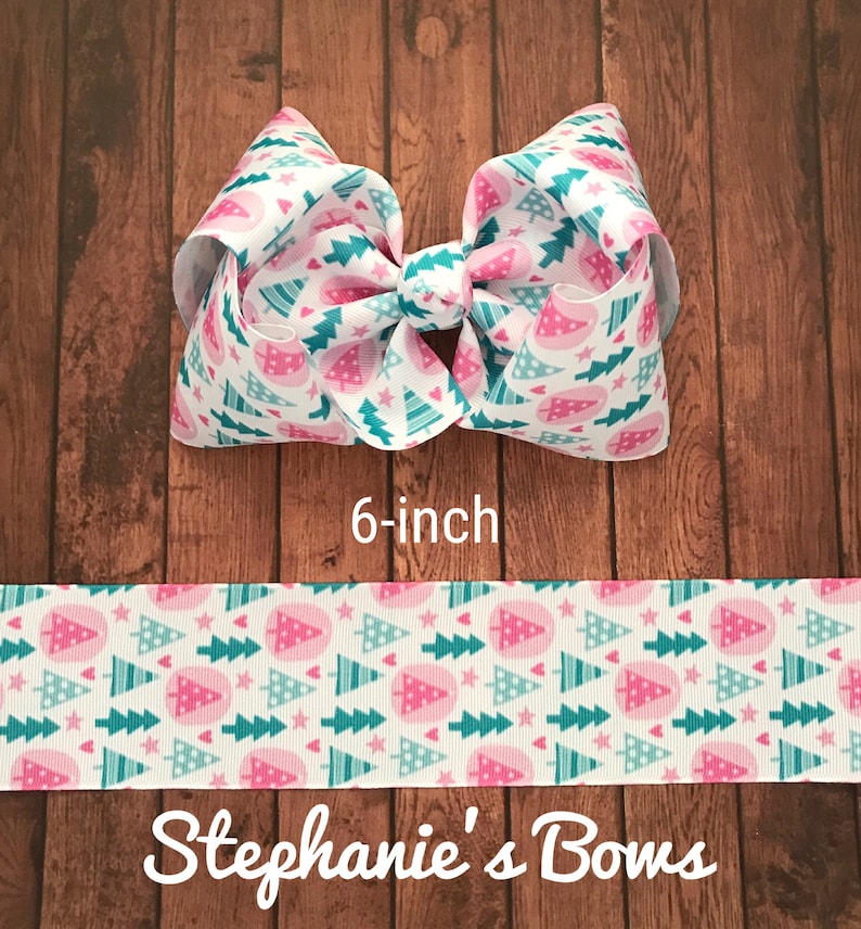 May include: A 6-inch hair bow with a white background and a repeating pattern of pink and teal Christmas trees. The bow is made of ribbon and has a large, layered design. The text "Stephanie's Bows" is at the bottom.