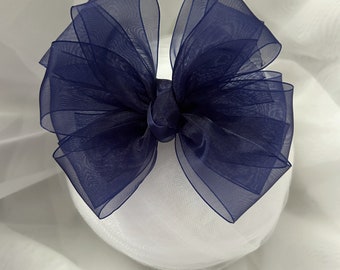 Könnte beinhalten: Eine große, marineblaue Schleife aus transparentem Stoff, wahrscheinlich für Haarschmuck oder Geschenkverpackungen. Die Schleife ist mehrlagig und voluminös, mit einem Knoten in der Mitte. Der Text "Stephanie's Bows" ist unten aufgedruckt.
