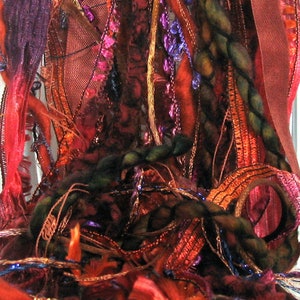 May include: A close-up of a colorful, textured fabric with a variety of ribbons and threads woven together. The fabric is primarily red, orange, and green, with hints of purple and gold.