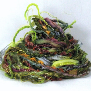 May include: A tangle of colorful yarn and ribbon in shades of green, purple, gold, and brown. The yarn is a mix of textures, including fuzzy, smooth, and sparkly.