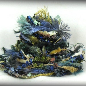 May include: A pile of colorful yarn scraps in shades of blue, green, gold, and brown. The yarn is arranged in a loose, messy pile, and some of the strands are tangled together.