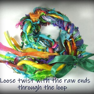 May include: A colorful, handmade wreath composed of various fabrics and ribbons in shades of pink, orange, yellow, green, blue, and purple. A green satin bow is attached. The text "Loose twist with the raw ends through the loop" is at the bottom.