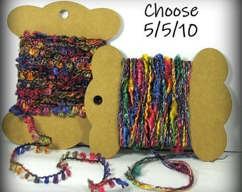 May include: Two spools of colorful yarn with metallic threads. The yarn is wound around cardboard spools with a heart-shaped cut-out. The text "Choose 5/5/10" is printed above the spools.