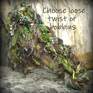 May include: A collection of textured art yarn in shades of green, brown, and gold, featuring various fabric strips, metallic threads, and fibers. The text "Choose loose twist or bobbins" is visible on the image, indicating available options.