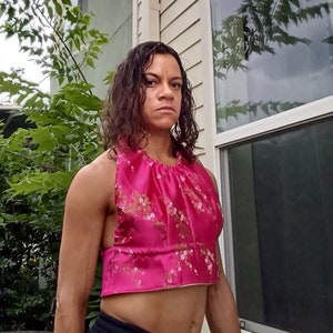 May include: A pink halter top with a floral print. The top is made of a silky material and has a gathered neckline.