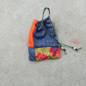 Könnte beinhalten: Eine kleine, gepatchte Kordeltasche mit einer grünen Schnur. Die Tasche ist aus Denim, Orange und Blumenstoff.