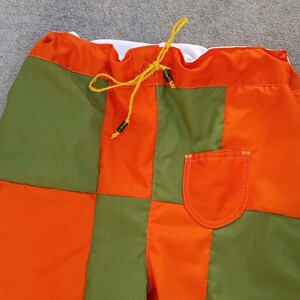 May include: Checkerboard patterned shorts with a drawstring waist and a single pocket. The shorts are made of a patchwork of orange and green fabric.