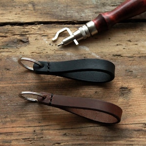 May include: Two leather keychains with silver key rings. The keychain on the left is black and the keychain on the right is brown.