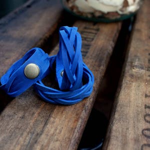 May include: Three blue leather bracelets with a braided design. One bracelet has a silver metal button.