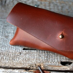 May include: A brown leather glasses case with a brass snap closure.