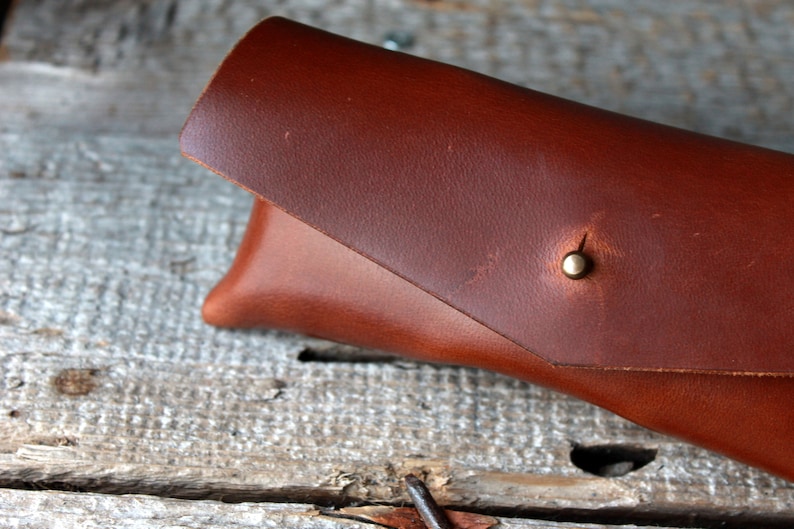 May include: A brown leather glasses case with a brass snap closure.