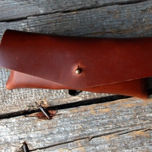 May include: A brown leather glasses case with a brass button closure.