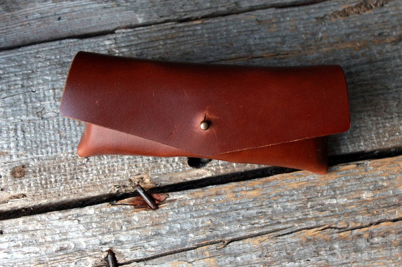 May include: A brown leather glasses case with a brass button closure.