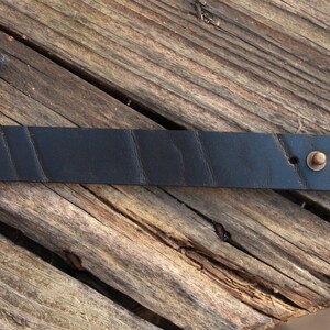 May include: A black leather bracelet with a brass buckle and three holes. The bracelet has a textured surface.