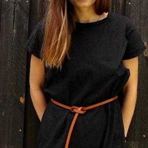 May include: A woman wearing a black dress with a brown leather belt tied in a knot. The belt is thin and has a long tail.