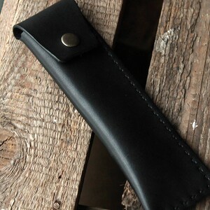 May include: A black leather pencil case with a metal button closure.
