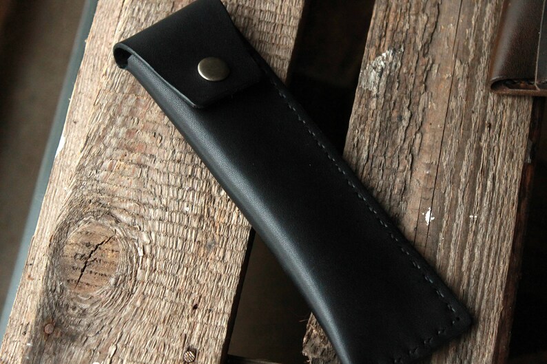 May include: A black leather pencil case with a metal button closure.