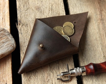May include: A brown leather coin purse with a triangular shape and a brass button closure. The purse is open and contains several gold coins.