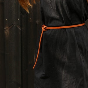 May include: A black dress with a brown leather belt tied in a knot at the front.