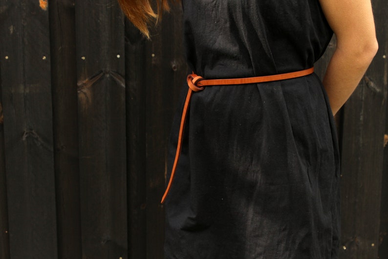 May include: A black dress with a brown leather belt tied in a knot at the front.