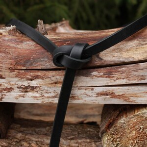 May include: A black leather strap tied in a knot around a piece of weathered wood.