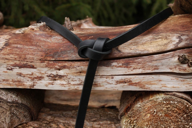 May include: A black leather strap tied in a knot around a piece of weathered wood.
