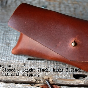 May include: A brown leather glasses case with a brass snap closure. The case is closed and measures 7 inches long and 2.7 inches high.