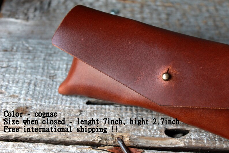 May include: A brown leather glasses case with a brass snap closure. The case is closed and measures 7 inches long and 2.7 inches high.