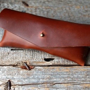 May include: A brown leather glasses case with a brass button closure.