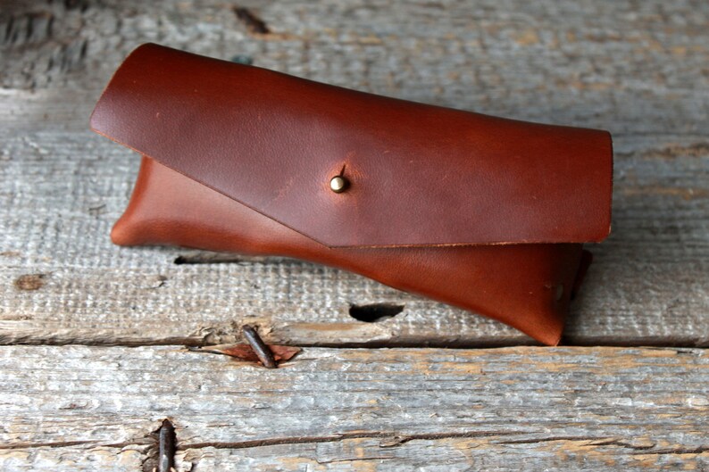 May include: A brown leather glasses case with a brass button closure.