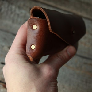 May include: A brown leather case with brass rivets. The case is folded closed and held in a hand.