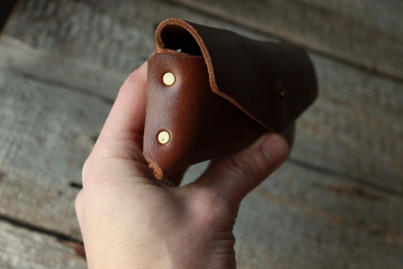 May include: A brown leather case with brass rivets. The case is folded closed and held in a hand.