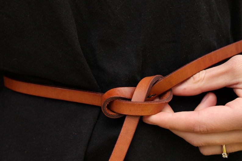 May include: A brown leather belt tied in a knot around a person's waist.