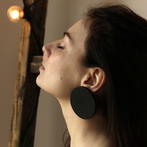 以下が含まれることがあります： 長い黒髪の女性が、大きな黒い丸いイヤリングをしています。イヤリングは滑らかでマットな素材で作られています。