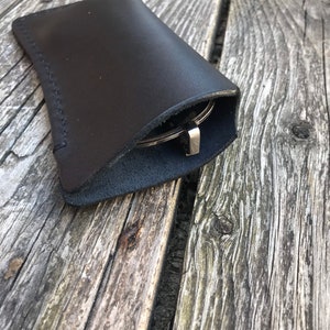 May include: A black leather glasses case with a stitched seam. The case is folded closed and the glasses are inside.
