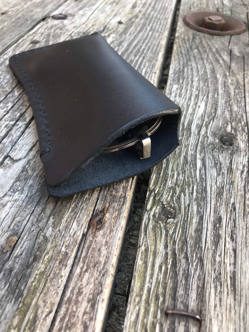 May include: A black leather glasses case with a stitched seam. The case is folded closed and the glasses are inside.