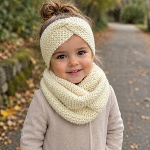 Peut inclure: Un bandeau tricoté de couleur crème avec un détail torsadé sur le devant et une écharpe infinie tricotée assortie de couleur crème. Les deux articles présentent un motif en tricot texturé et sont portés sur un manteau beige clair.