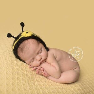 May include: A newborn baby wearing a black and yellow crocheted bee hat with antennae, sleeping on a yellow blanket.