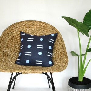 May include: A blue and white geometric patterned throw pillow on a woven wicker chair with a green plant in a black and white striped pot.