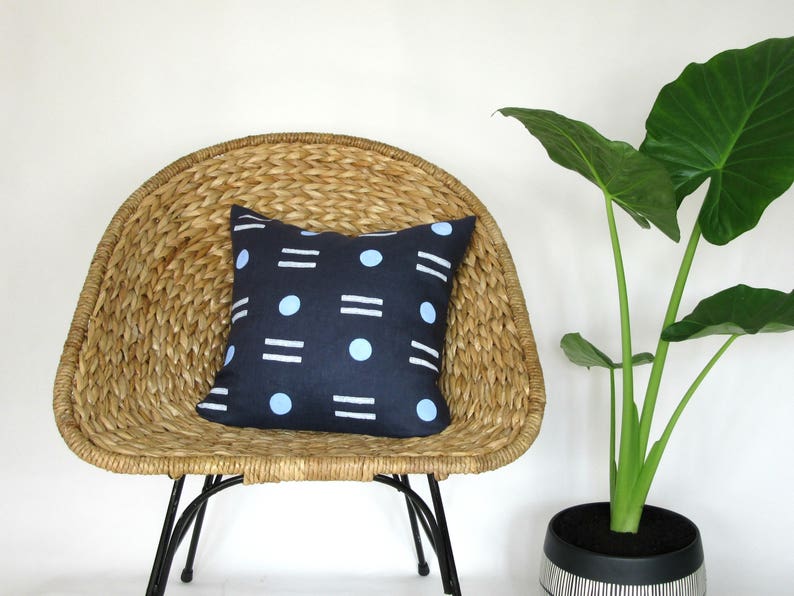 May include: A blue and white geometric patterned throw pillow on a woven wicker chair with a green plant in a black and white striped pot.