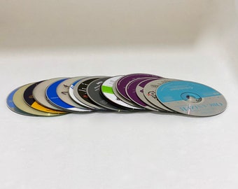 May include: A stack of 14 silver compact discs with various colorful labels. The discs are arranged in a semi-circle with the top disc facing the camera.