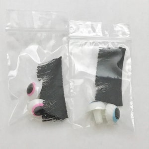 May include: Two clear plastic bags containing craft supplies. One bag contains black craft fur and two pink and black googly eyes. The other bag contains black craft fur and two white googly eyes with blue pupils.