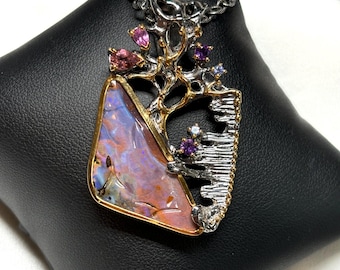 May include: A silver and gold-tone pendant necklace with a large, colourful opal stone. The pendant has a tree-like design with pink, purple, and blue gemstones. The necklace is displayed on a black surface.