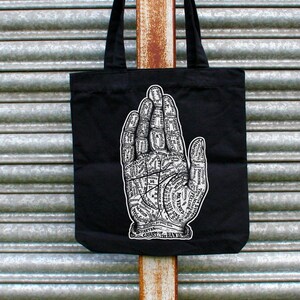 May include: Black tote bag with a white illustration of a hand with lines and markings. The text "CHIROMANCY" is printed below the hand.