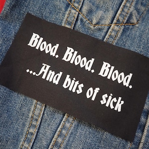 Könnte beinhalten: Ein schwarzer Aufnäher mit weißem Text "Blood. Blood. Blood. ...And bits of sick" in gotischer Schrift ist auf eine blaue Jeansjacke genäht.
