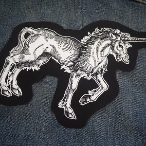 May include: A black and white embroidered patch of a unicorn with a long horn, on a blue denim background.