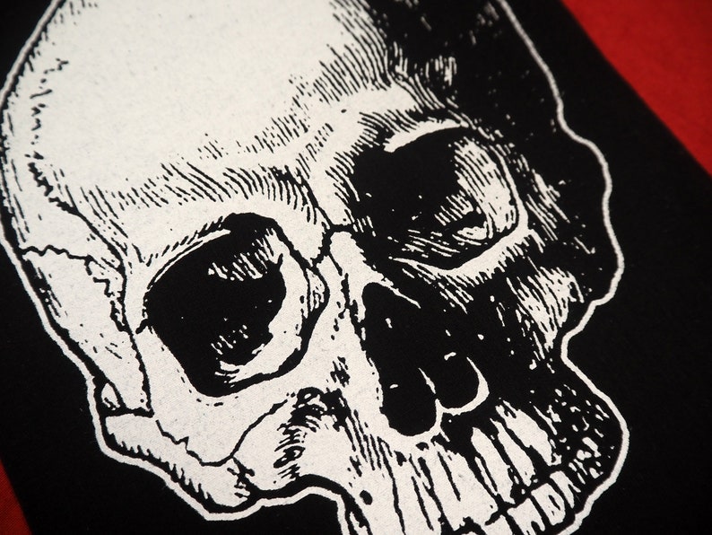May include: A black and white illustration of a human skull. The skull is drawn in a detailed, realistic style, with visible teeth and eye sockets.
