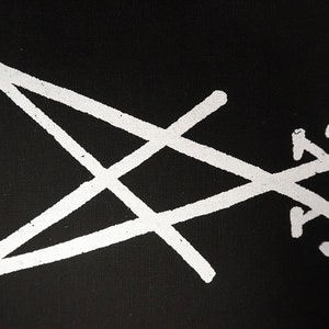 K&ouml;nnte beinhalten: Wei&szlig;es, stilisiertes Sigill auf schwarzem Hintergrund. Das Design zeigt ein Dreieck, ein Kreuz und eine Reihe geschwungener Linien. Das Bild hat ein strukturiertes Aussehen, das auf einen Druck oder eine bemalte Oberfl&auml;che hindeutet. Die Gesamt&auml;sthetik ist minimalistisch und symbolisch.